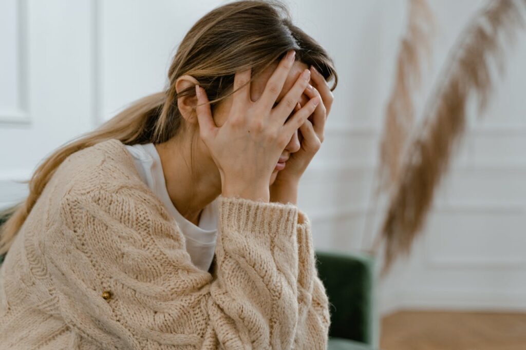 A woman sitting indoors covering her face in frustration, depicting stress and mental health challenges.