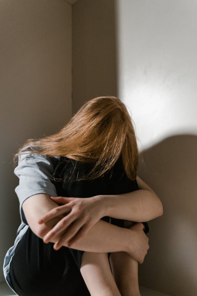 A woman sits alone in a corner, reflecting anxiety and solitude. Soft lighting accentuates her posture.